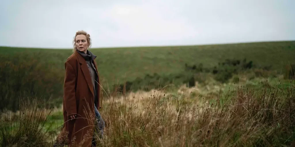 A woman stands in the grass and looks to her right in a still from the movie Unmoored