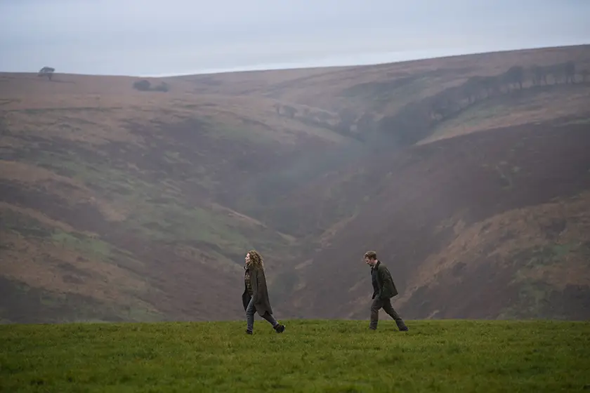 A woman and a man walk one behind the other in the mountains in a still from the movie Unmoored