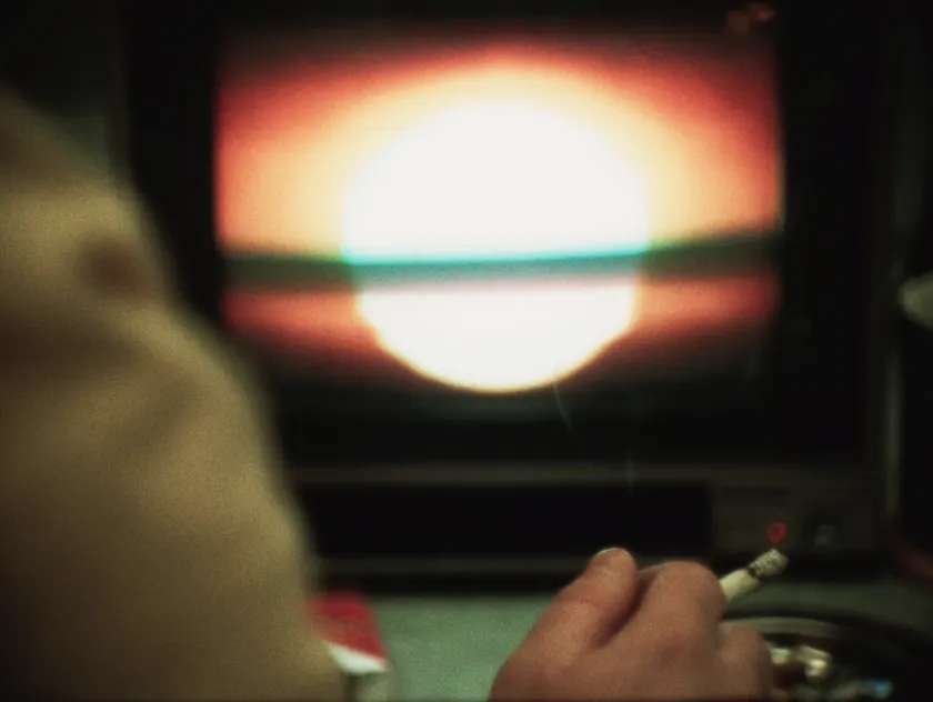 A person holds a cigarette while watching a blurry red screen in a still from the film Levers
