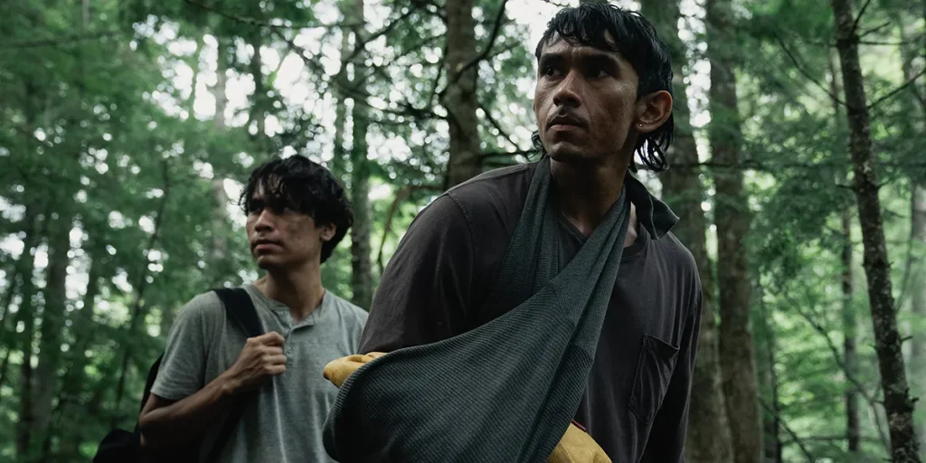 Two young men are in a forest in a still from the film At the Place of Ghosts (Sk+te'kmujue'katik)