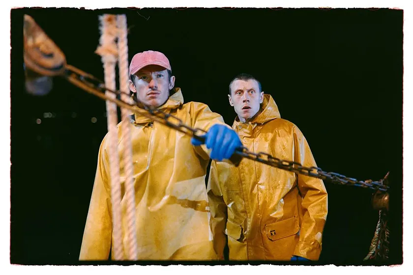 George MacKay and Callum Turner wear yellow fishing overalls in a still from Rose of Nevada, by Mark Jenkin, featured in a Loud And Clear Reviews interview
