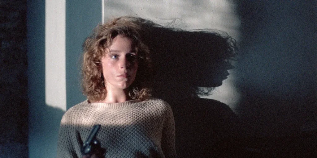 Frances McDormand holds a gun while leaning against a wall in the movie Blood Simple