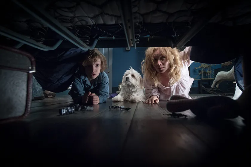 A woman, a boy and a dog look under the bed in a still from The Babadook, one of the 10+ movies to watch on Halloween 2025 this year according to Loud And Clear Reviews