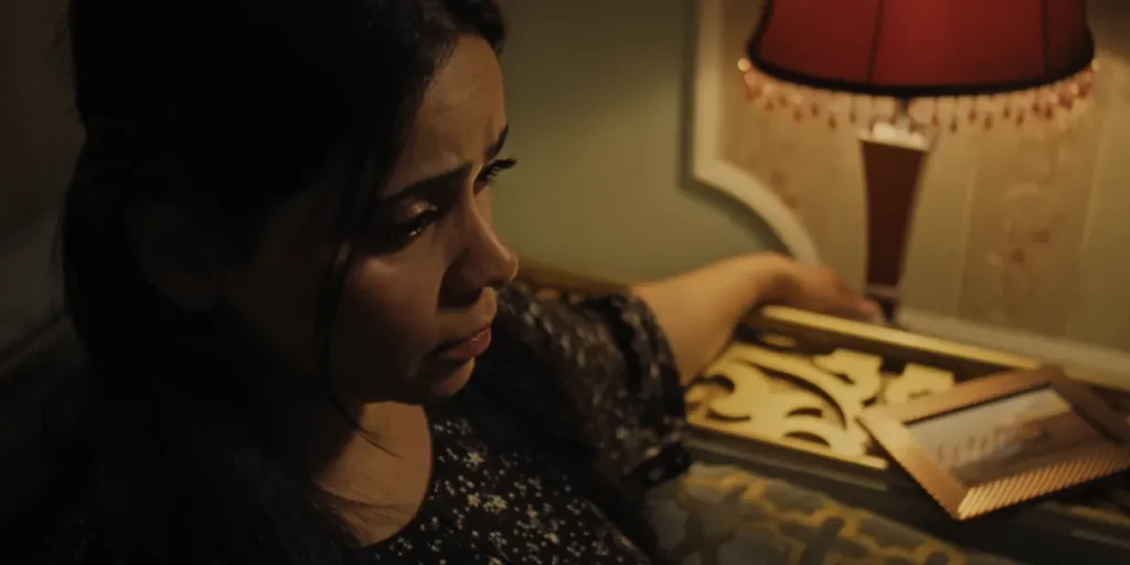 A woman leans on a desk in a still from The Vile