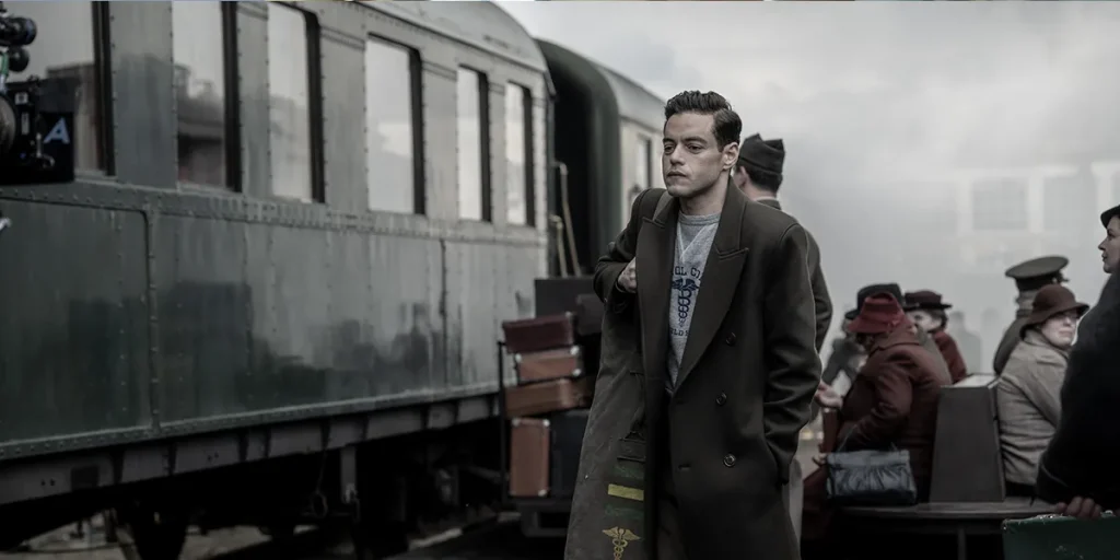 Rami Malek stands by a train in the movie Nuremberg