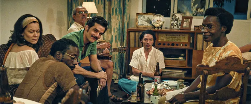 Wagner Moura sits surrounded by other people in a house in The Secret Agent (O Agente Secreto), whose ending and true impact is explained in this article