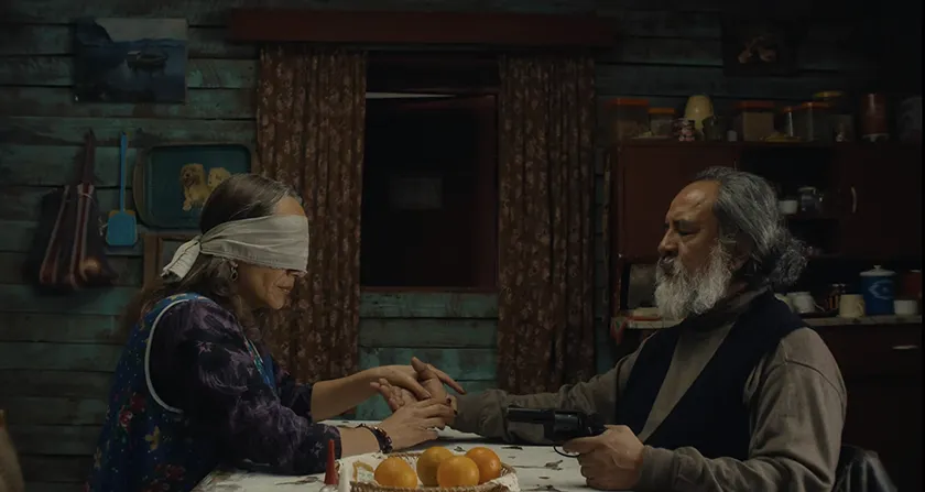 A man holds a blindfolded woman's hand at the dinner table in The Mysterious Gaze of the Flamingo