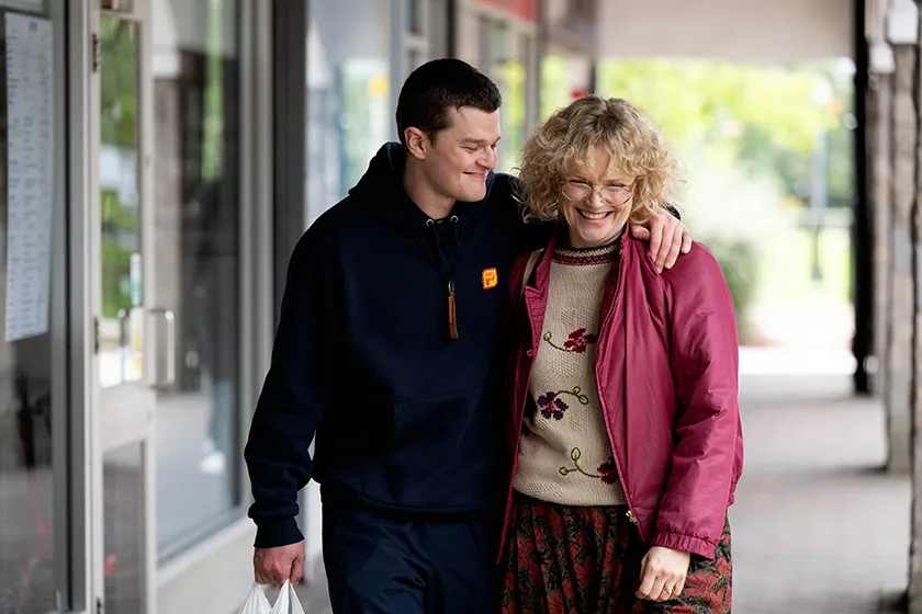 Robert Aramayo, whom we interview alongside Kirk Jones, and Maxine Peake hug while walking in a still from I Swear