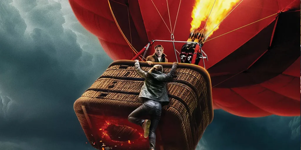 [L-R] Hera Hilmar as “Emmy,” is falling out of a air hot balloon mid-air and Jeremy Irvine as “Zach” is holding onto her in the poster for the movie Turbulence