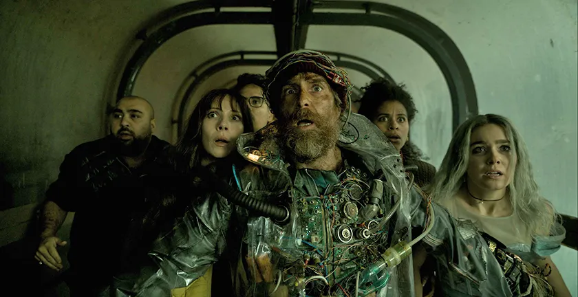 Five people stand behind a man wearing steampunk clothes with tubes coming out of them and a see-through raincoat in a still from Good Luck Have Fun Don't Die