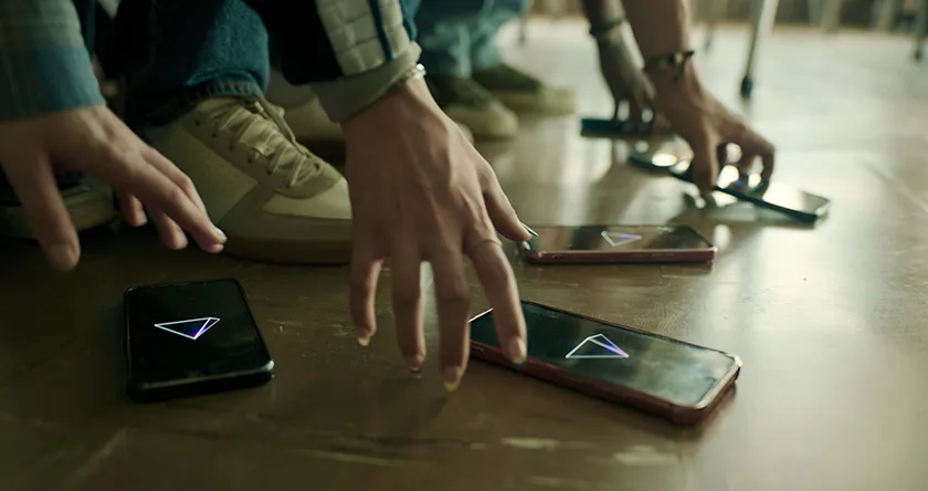 Teenagers grab phones with a triangle on the screen in a scene from Good Luck, Have Fun, Don't Die, whose DOP, James Whitaker, we interview