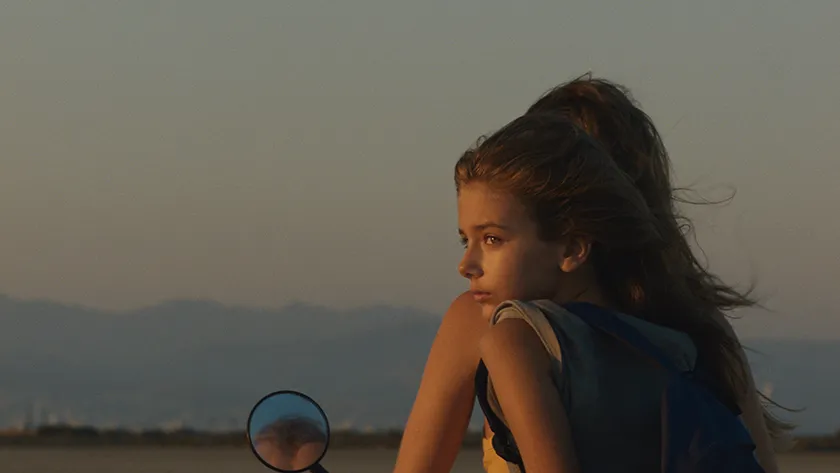 A young girl on a bike turns around looking sad in a still from the 2026 movie Hold Onto Me (Κράτα Με)