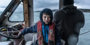 A young boy on a boat looks straight into the camers in a still from Bucks Harbor