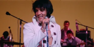 Elvis Presley sings and smiles wearing a white suit in a still from EPiC: Elvis Presley in Concert