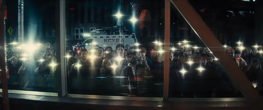 A crowd stands pointing smartphone flashlights at a window in a scene from Disclosure Day, which this article tells us everything we know about