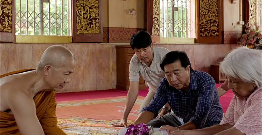 A buddhist monk and three people sit on the floor in a monastery in a still from the film 9 Temples to Heaven
