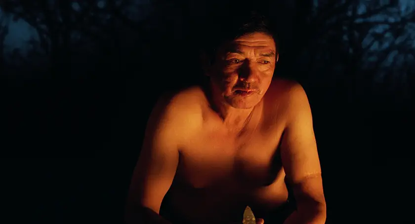 Misael Saavedra, whom we interview with director Lisandro Alonso, sits by the fire in a nighttime still from the movie Double Freedom (La Libertad Doble)