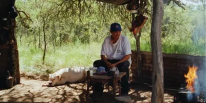 Misael Saavedra sits outdoors with a dog behind him in a still from Lisandro Alonso's Double Freedom (La Libertad Doble)