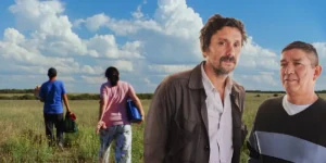 Lisandro Alonso and Misael Saavedra, whom we interview, pose for a photo at Cannes. Behind them, on their right, is a still from their movie Double Freedom (La Libertad Doble) depicting two people walking away on some grass