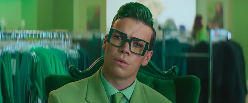 Will Poulter wears a green suit with green hair and glasses in I Love Boosters