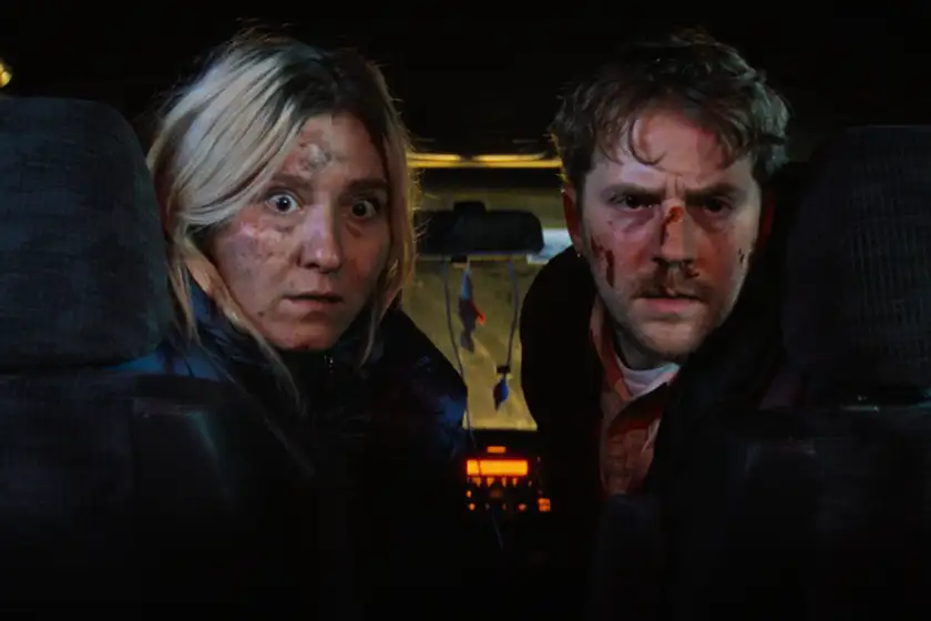 A man and a woman in a car look behind them with a scared expression and their faces covered in blood in a still from the 2026 film Big Break