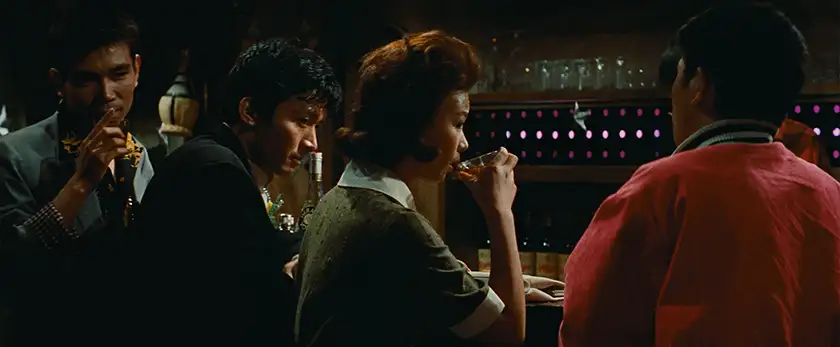 A woman drinks at a bar while three men look at her in a still from Cruel Story of Youth