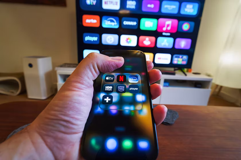 Hand holding smartphone controlling smart TV apps (Jakub Żerdzicki, Unsplash)