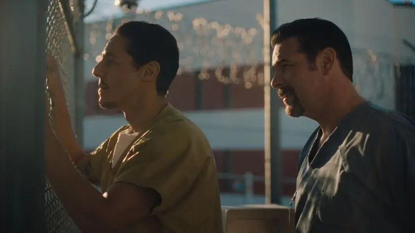 A man stands behind another man who is leaning against a net in a still from the movie Bruton