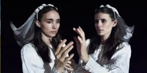 Kate Mara and Rooney Mara almost touch hands while wearing a wedding dress against a black background in a still from the movie Bucking Fastard