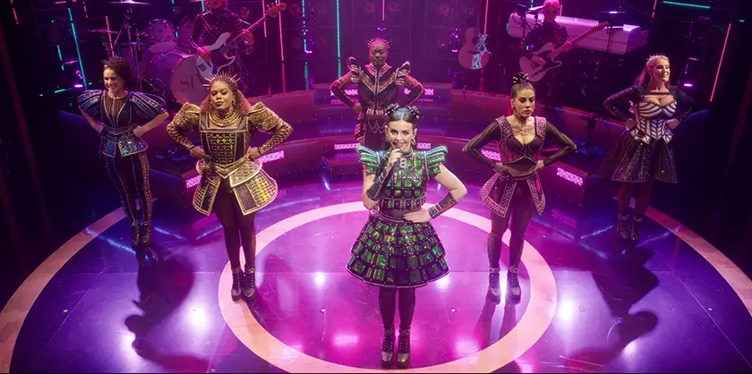 The six wives stand on the stage while one of them sings in a still from Six the Musical Live!