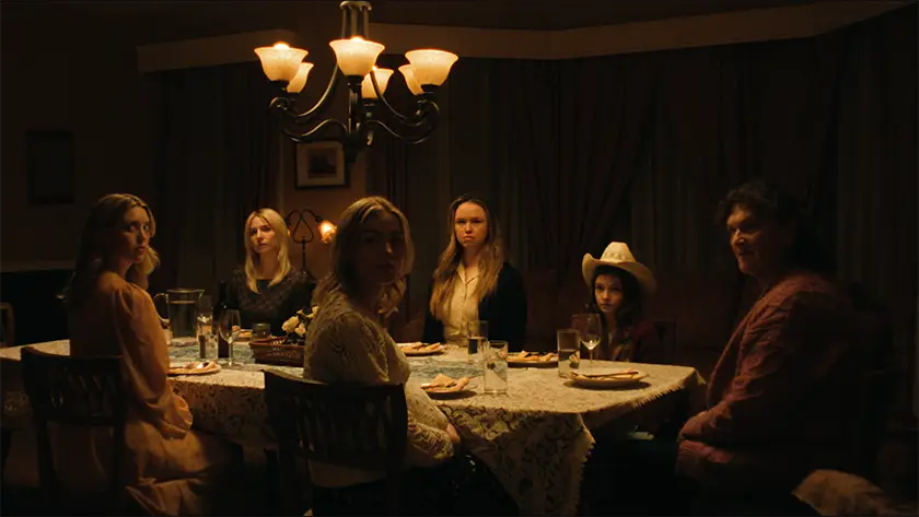 People sit at the dinner table in a dim light in a still from the film Breeder